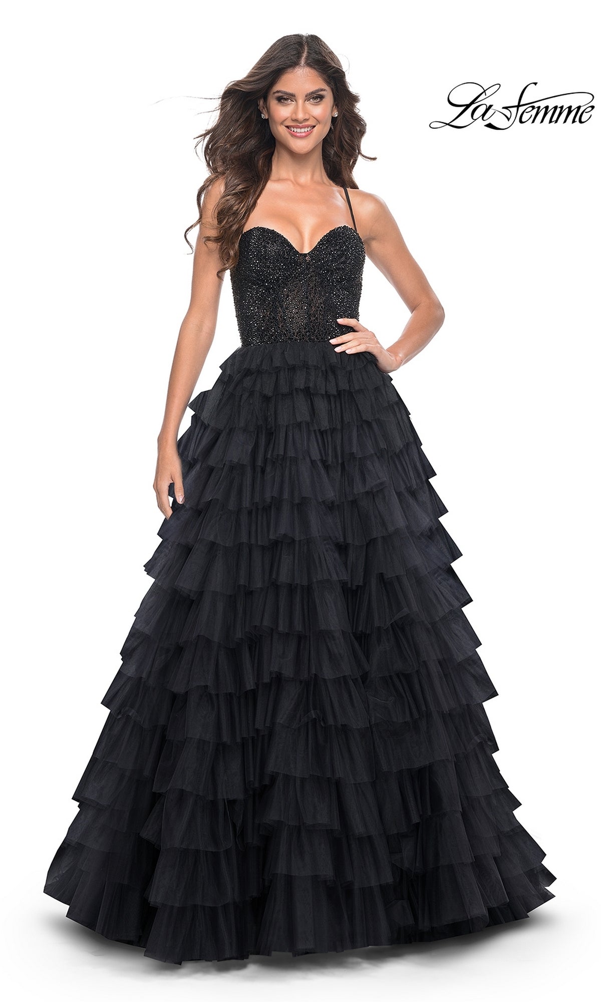 A woman stands and smiles in the La Femme Long Ruffled Prom Ball Gown 32002, featuring a black sparkling A-line design with a fitted bodice and flowing ruffled skirt, set against a white background.